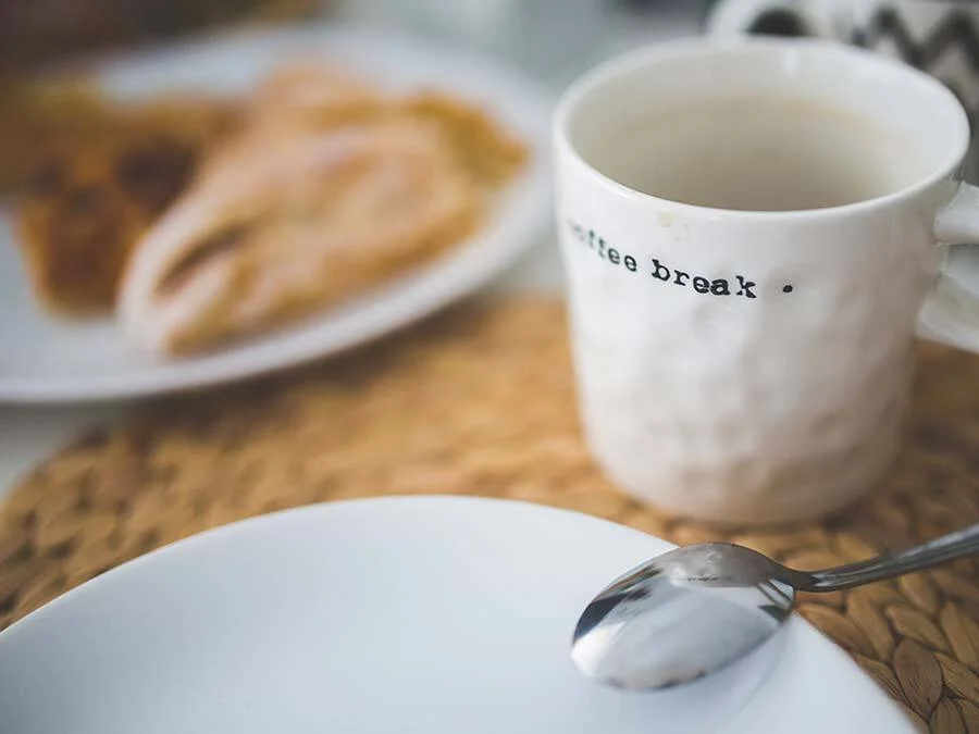 Eine Kaffeetasse und ein leerer Teller stehen auf einem Tisch.