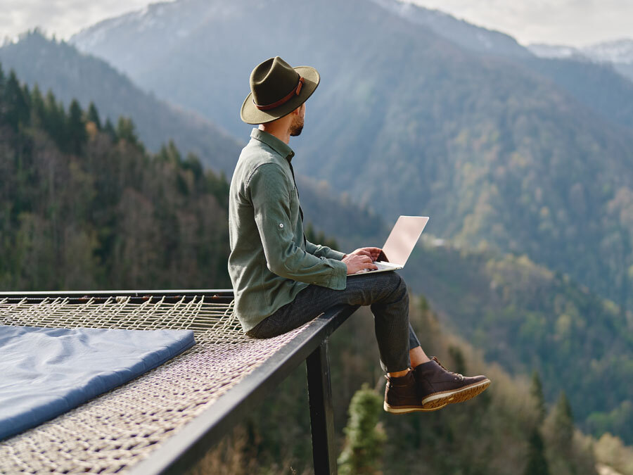 Ein Mann sitzt in den Bergen auf einer Hängematte, während er Homeoffice in Ausland betreibt.
