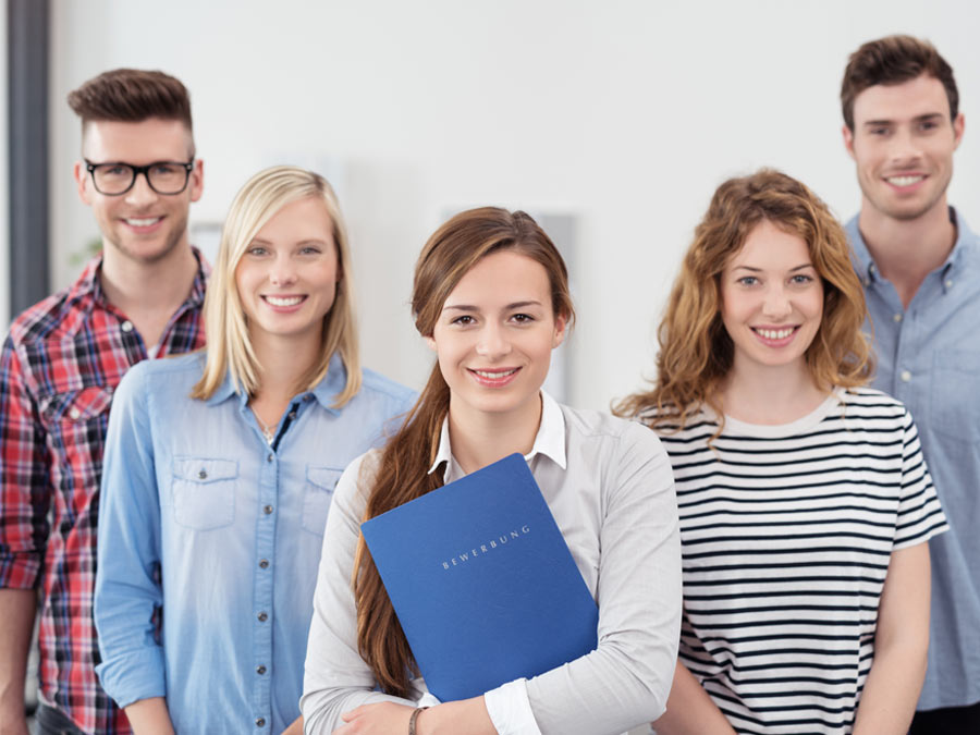 Drei junge Frauen und zwei junge Männer stehen nebeneinander und halten Bewerbungsmappen in der Hand.